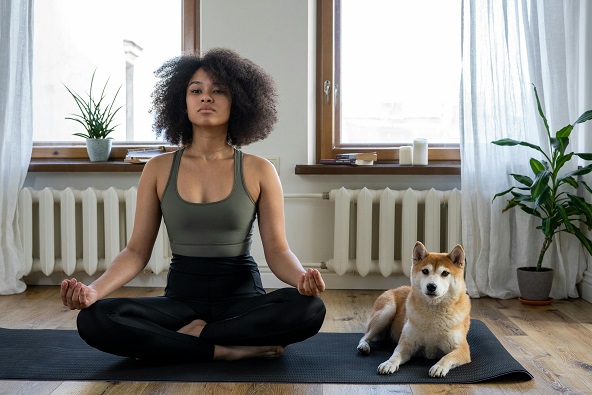 Black woman meditating with a dog on a yoga mat